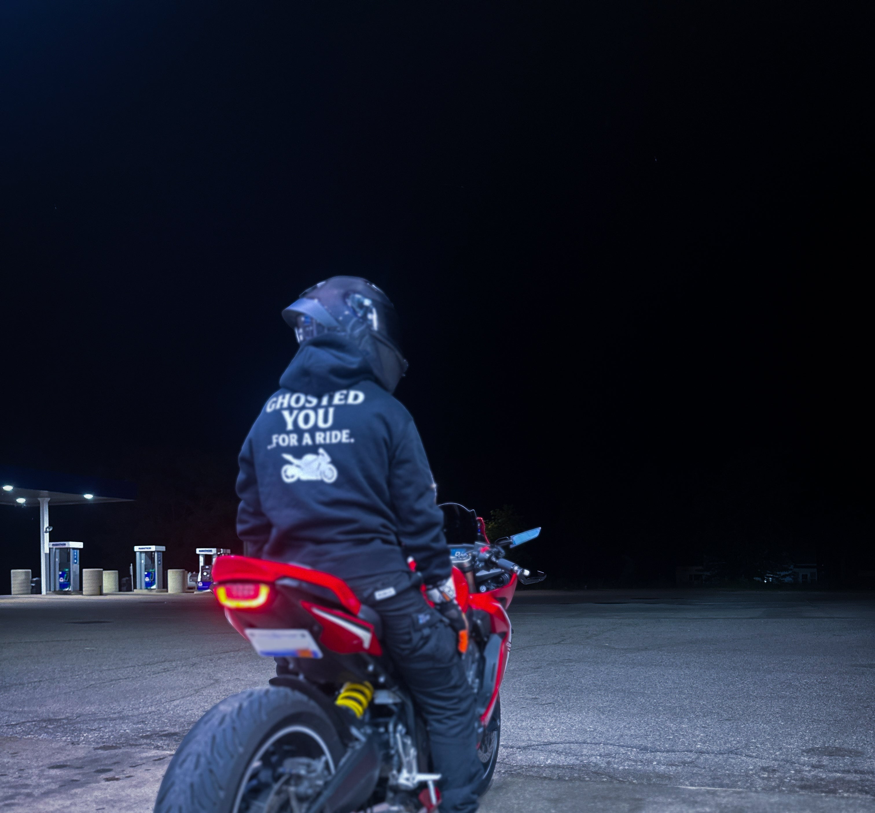 Person standing next to a red motorcycle at night with a dark background
